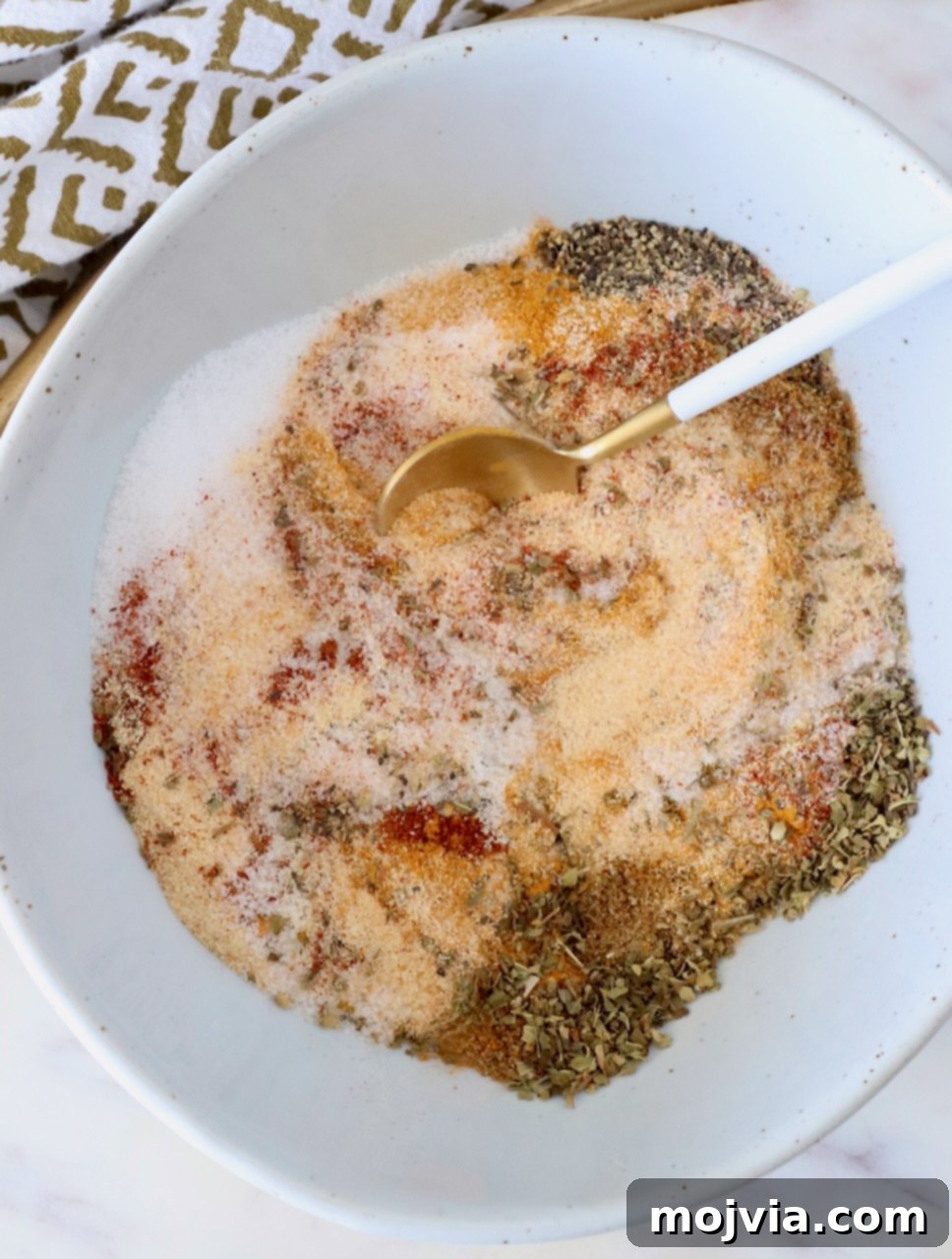 Adobo Spice Blend 2 various dried herbs and spices mixed together in a bowl with a small spoon, showcasing the vibrant colors and textures of the blend