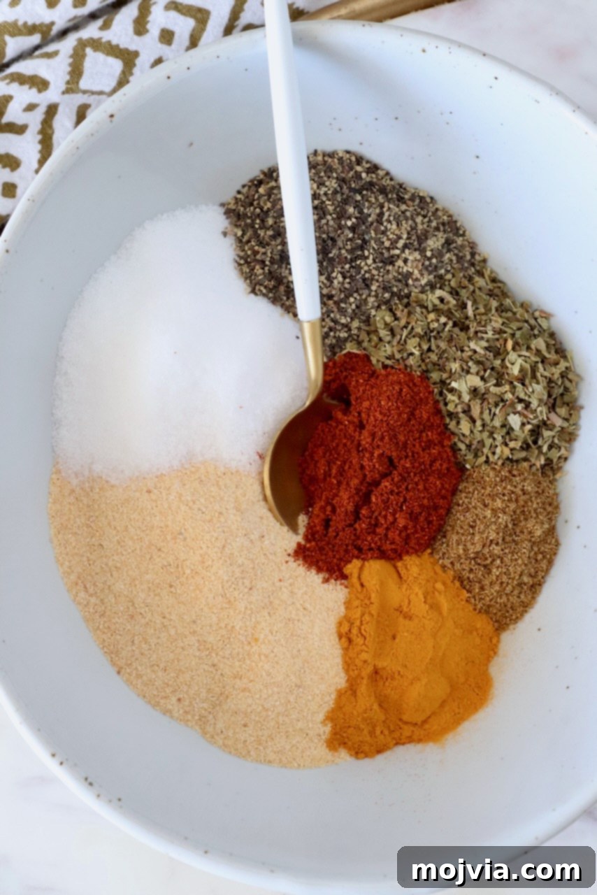 Adobo Spice Blend 5 dried herbs and spices separated in a bowl with a spoon, showing the individual ingredients before mixing