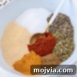 Adobo Spice Blend 6 dried herbs and spices separated in a bowl with a spoon, highlighting the individual components of Adobo seasoning