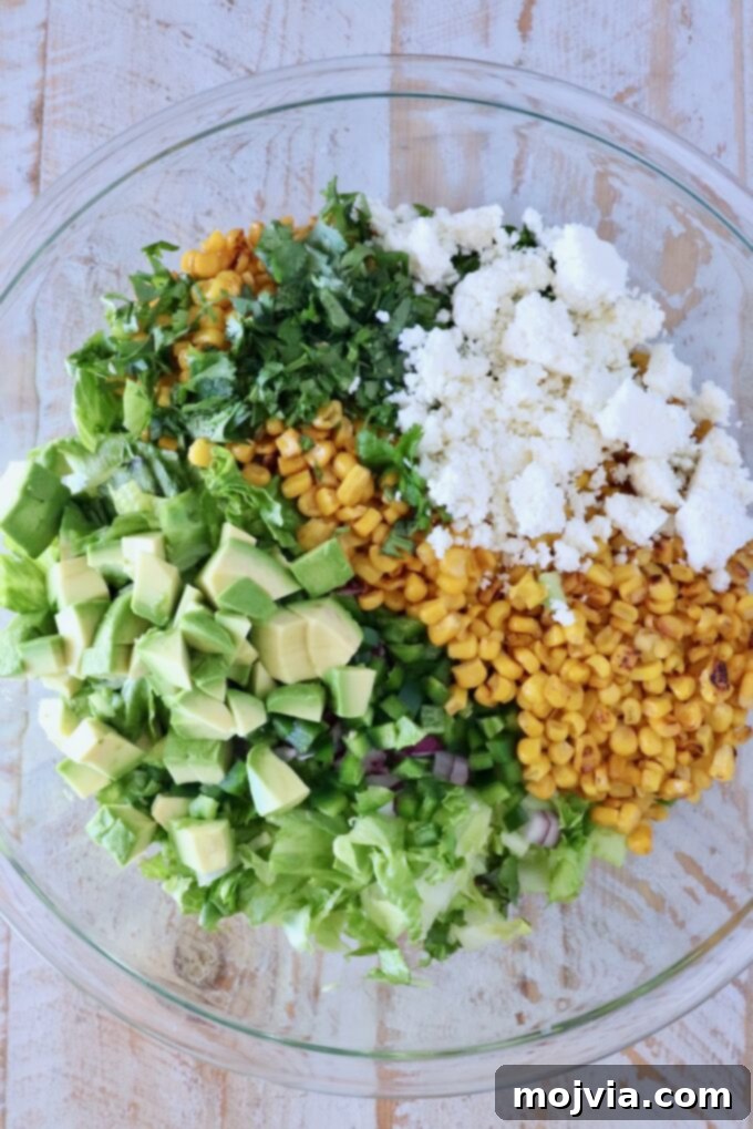 Esquites Style Corn Salad 7 corn, avocado, cotija cheese, cilantro and chopped lettuce in a large glass bowl