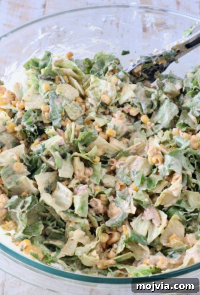 Esquites Style Corn Salad 9 tossed street corn salad in a large glass bowl with kitchen tongs