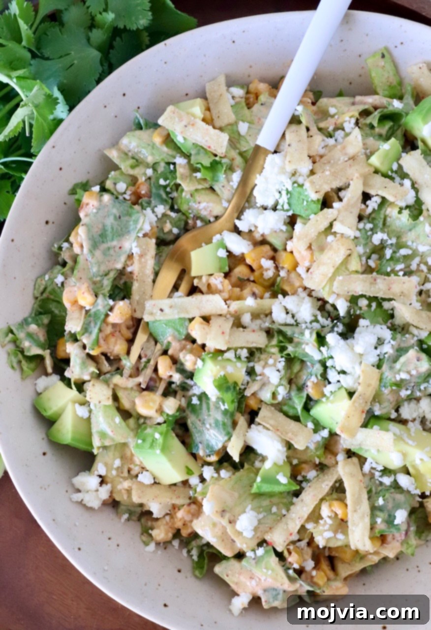 Esquites Style Corn Salad 10 street corn salad in a bowl with a fork, topped with tortilla strips