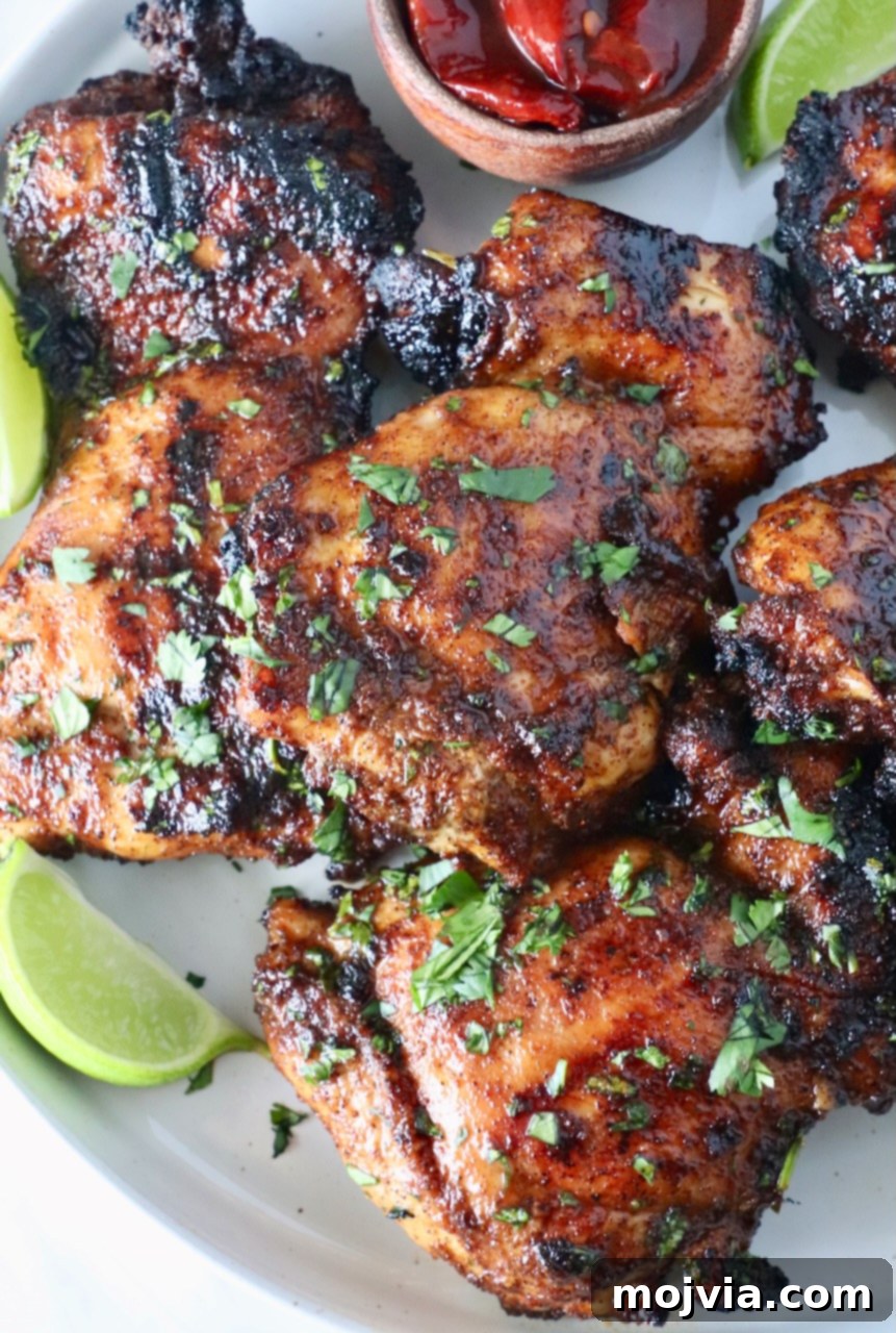 Chipotle Honey Glazed Chicken 2 glazed grilled chicken thighs stacked up on a plate with fresh cilantro and lime wedges, showcasing the smoky honey glaze