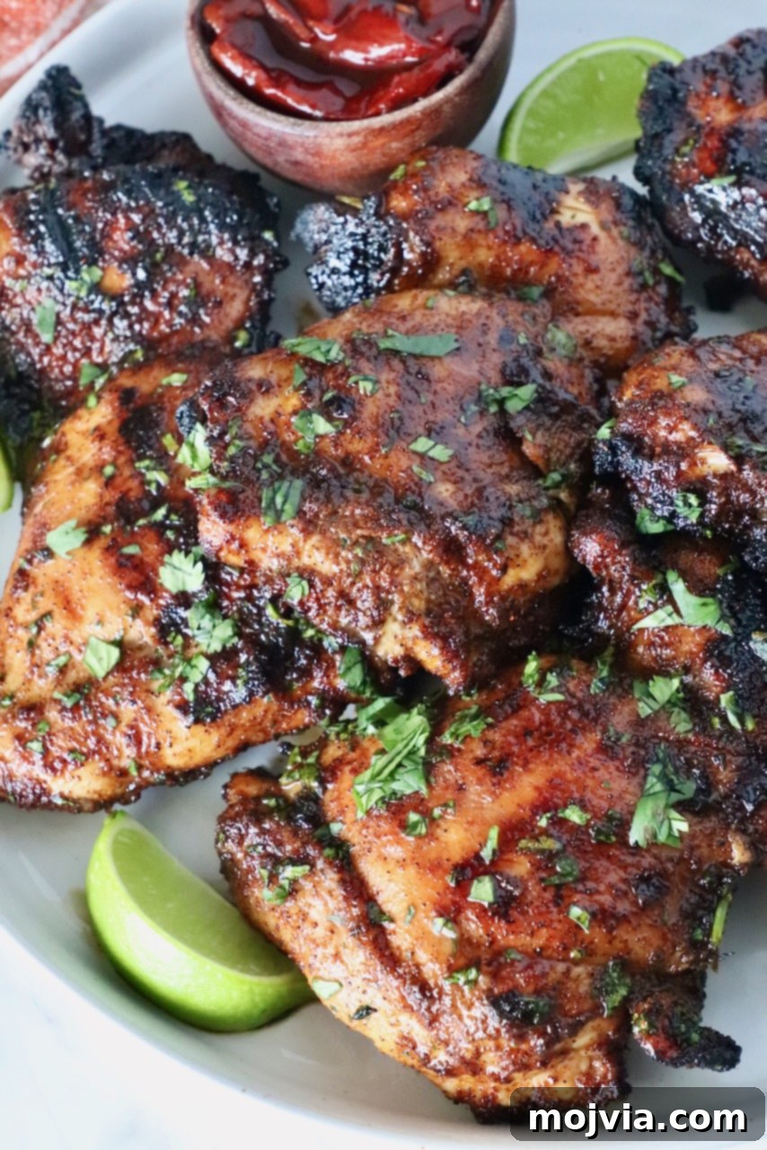 Chipotle Honey Glazed Chicken 11 grilled chicken thighs stacked up on a plate with lime wedges and chipotle peppers in a small wooden bowl, emphasizing the main dish