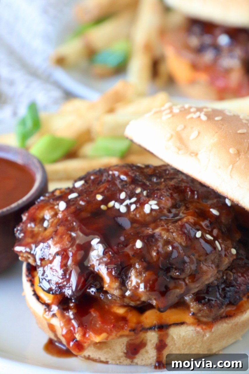 A Korean BBQ Burger, perfectly assembled on a bun and presented on a plate, with the top bun artfully leaned on the side