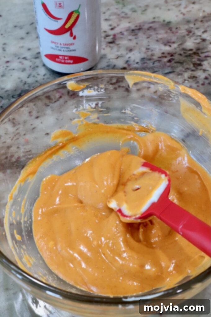 Gochujang mayonnaise being prepared in a glass bowl with a red spatula