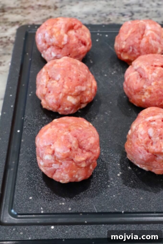 Seasoned balls of ground beef and pork ready for smashing on a cutting board