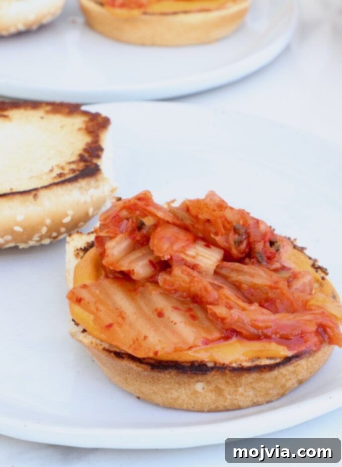 A hamburger bun on a plate, generously topped with gochujang mayo and fresh kimchi
