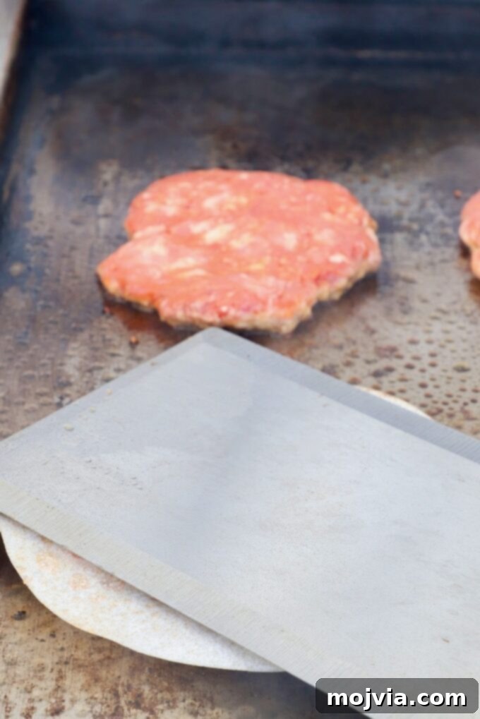 Burger patty being smashed flat with a large metal spatula on a hot griddle