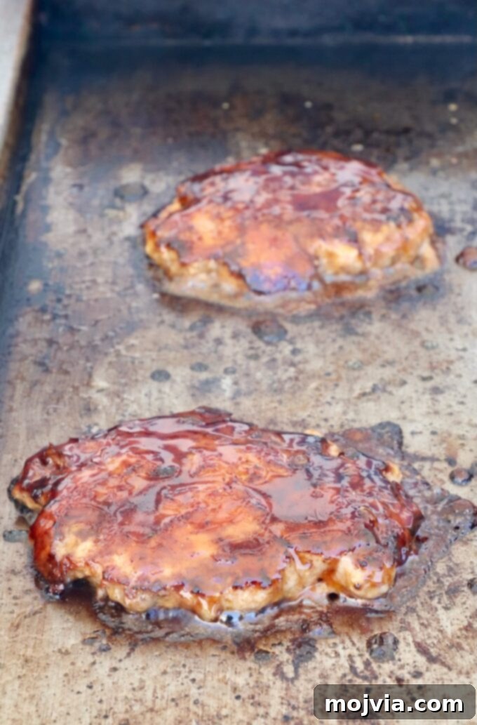 Burger patties coated with Korean BBQ sauce on a griddle, glistening under the heat
