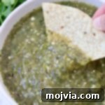 Verde Zing Salsa 10 tomatillo salsa in a bowl with a hand dipping a tortilla chip in the salsa