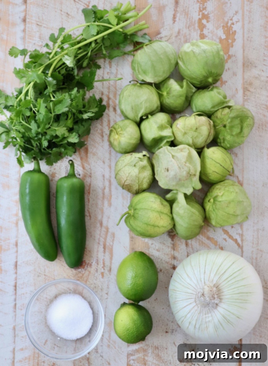 Verde Zing Salsa 3 Fresh ingredients for tomatillo salsa, including green tomatillos, jalapeños, white onion, and cilantro, laid out on a white wooden board.