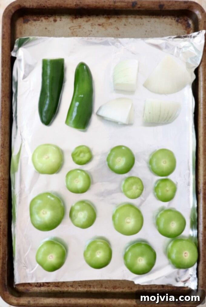 Verde Zing Salsa 4 Fresh whole tomatillos, white onion quarters, and whole jalapeño peppers laid out on a foil-lined baking sheet, ready for roasting.