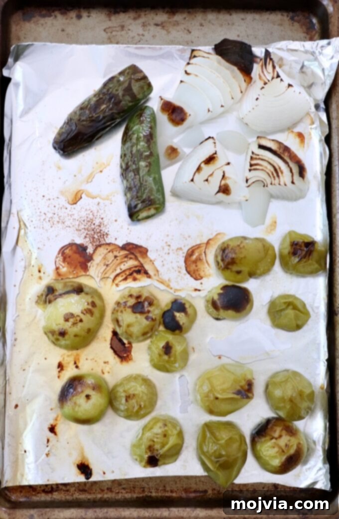 Verde Zing Salsa 5 Roasted tomatillos, white onion, and jalapeños on a foil-lined baking sheet, showing a slight char and softened texture after broiling.