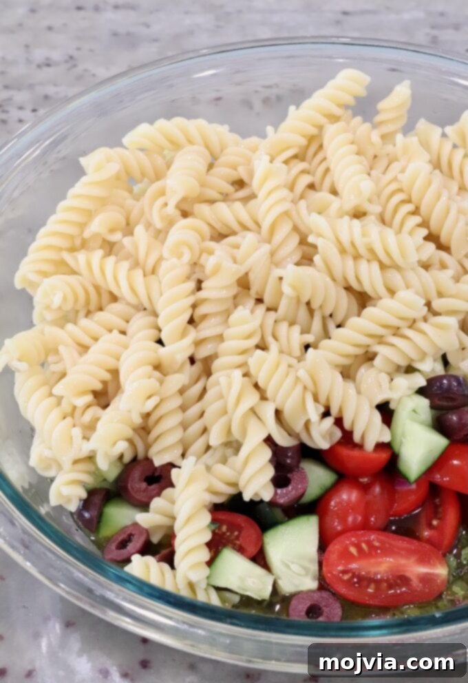 Aegean Breeze Pasta Medley 7 cooked rotini pasta, diced cucumber, tomatoes and olives in a large glass bowl