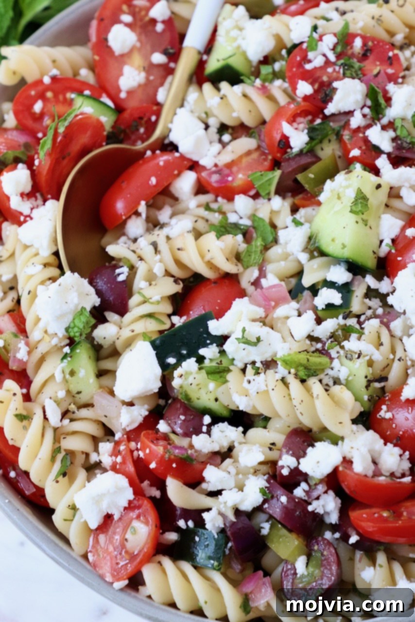Aegean Breeze Pasta Medley 8 pasta salad topped with crumbled feta cheese in a bowl with a spoon