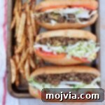 The Ultimate Chopped Cheese 9 Three chopped cheese sandwiches with sliced tomatoes and shredded lettuce lined up on a baking sheet with seasoned french fries on the side