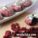 Sumptuous Red Velvet Kisses 2 Red Velvet Kiss Cookies adorned with melted Hershey's Hugs, showcasing their vibrant red color and powdered sugar crinkle.