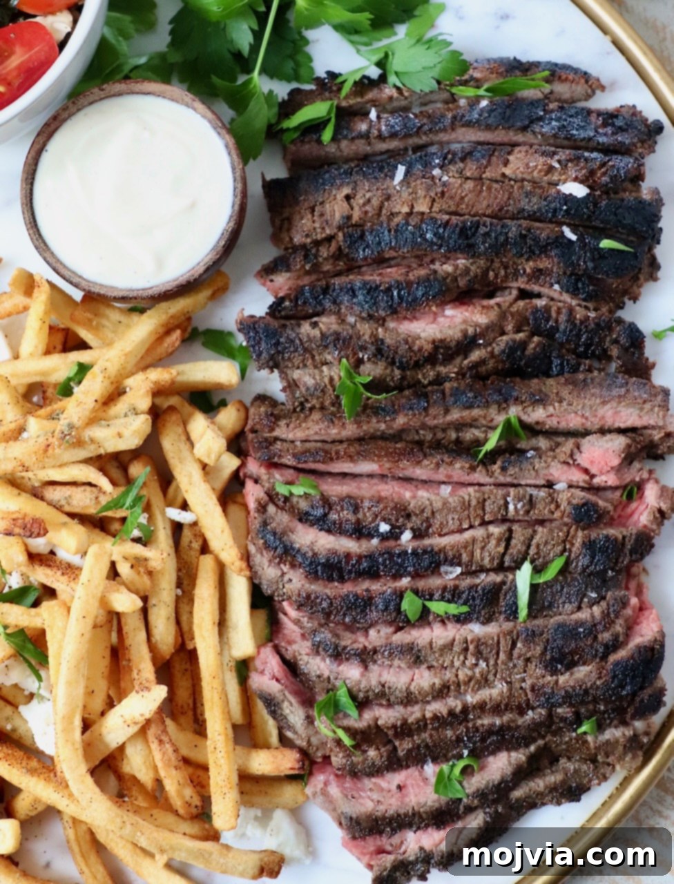 Sliced, grilled beef shawarma served on a platter with golden french fries and a small bowl of creamy garlic sauce. The beef is beautifully caramelized and ready to be enjoyed.