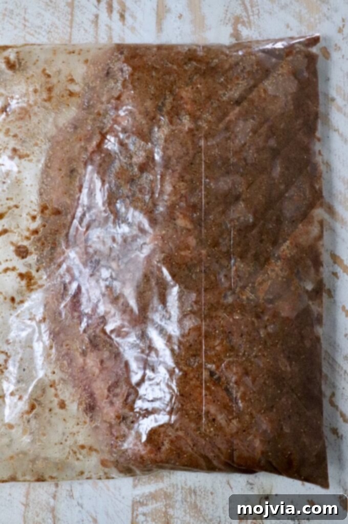 A raw skirt steak marinating generously in a vibrant shawarma seasoning blend, olive oil, lemon juice, and red wine vinegar inside a large plastic zipper bag. The beef is fully coated, promising rich flavor.