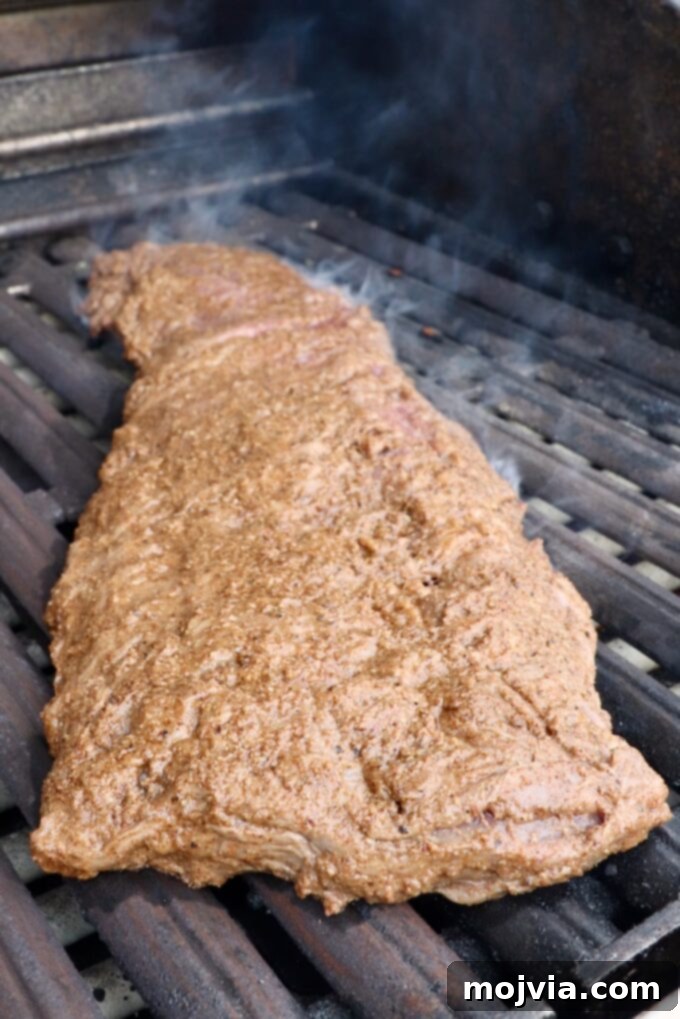 A beautifully marinated skirt steak cooking on a hot grill, showing distinct grill marks beginning to form. The edges are crisping, indicating a perfect sear.