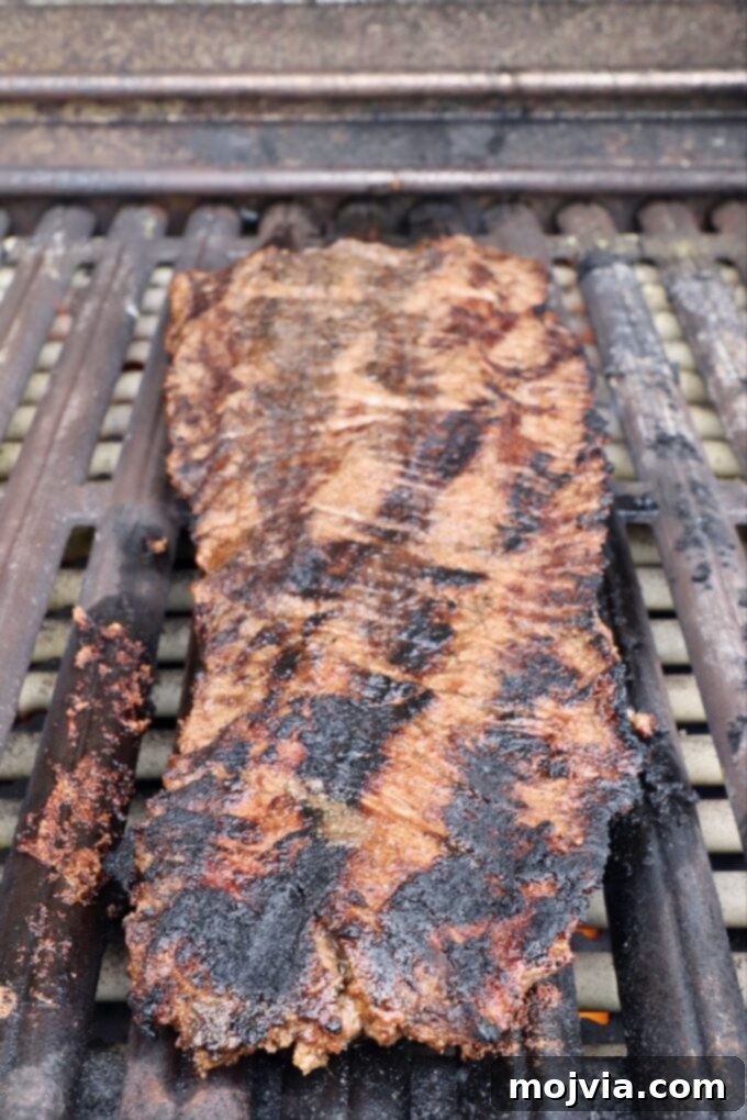 A perfectly grilled skirt steak resting on the grill, fully cooked with excellent charring and rich brown color. It's ready to be removed and rested before slicing.