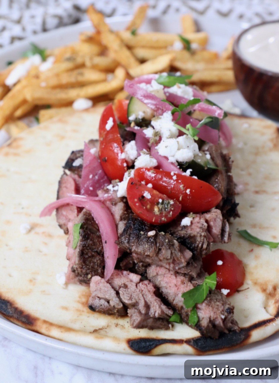 Sliced, grilled beef shawarma piled high on warm pita bread, generously topped with fresh diced tomatoes, thinly sliced red onions, and crumbled feta cheese. Served alongside golden french fries for a complete meal.