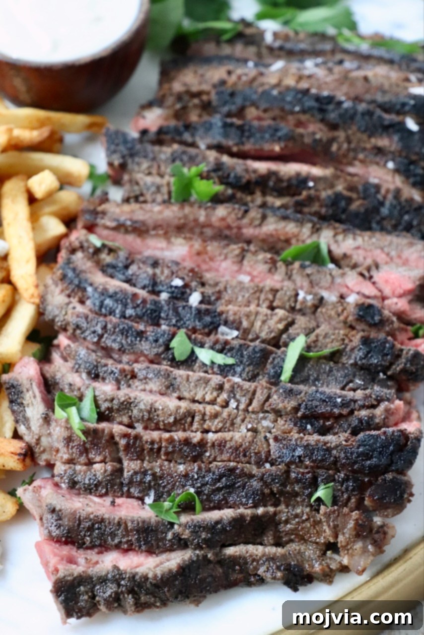 A generous serving of thinly sliced beef shawarma presented on a elegant platter, accompanied by a side of crispy french fries and a small, inviting bowl of creamy dipping sauce.