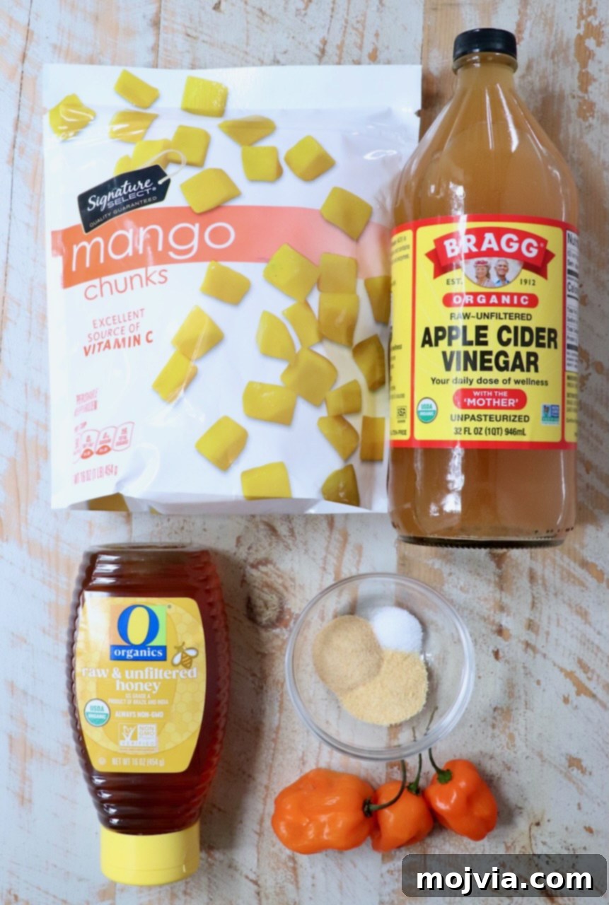 Fresh ingredients for mango habanero sauce laid out on a white wooden board, including diced mango, habanero peppers, honey, and spices