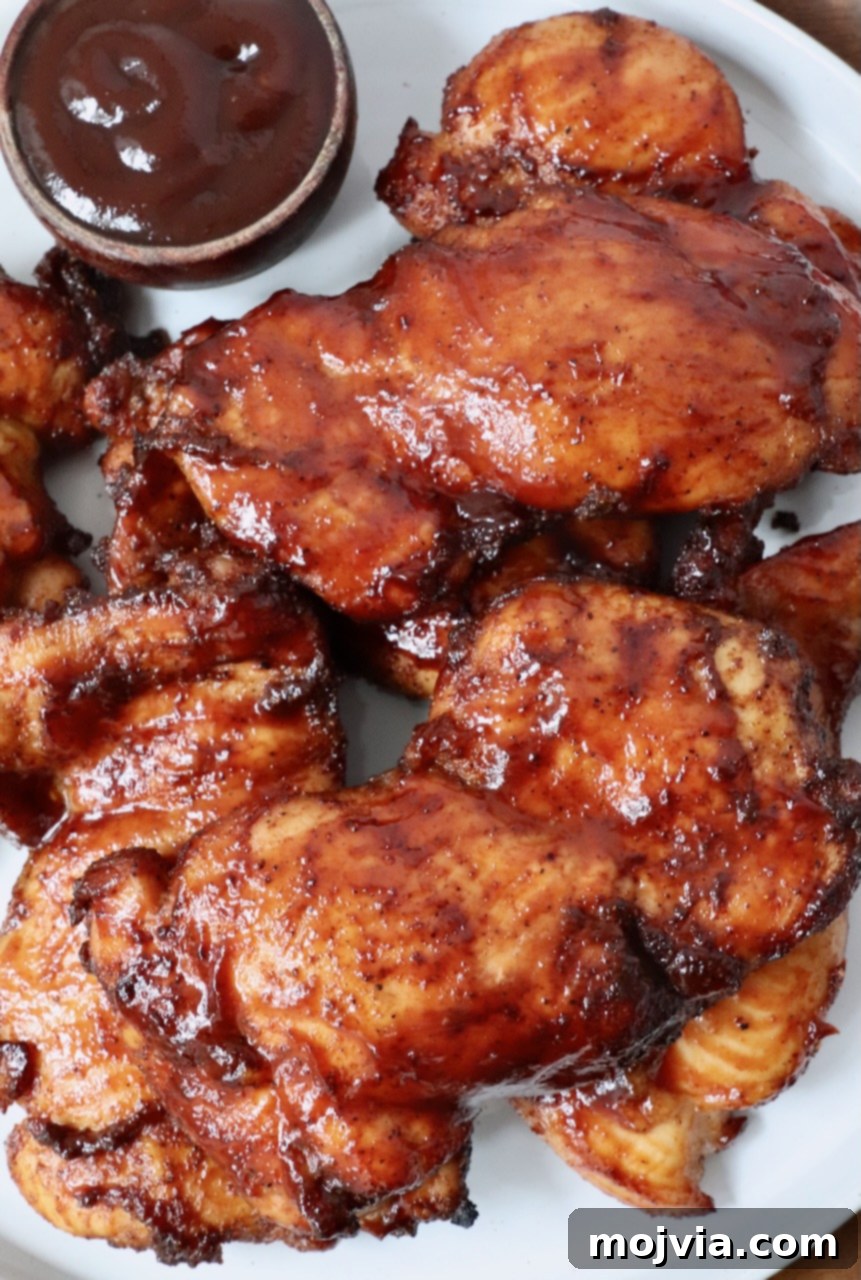 Perfectly Smoked Chicken Thighs 2 smoked chicken thighs glazed with bbq sauce stacked up on a plate with a small bowl of bbq sauce on the side