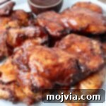 Perfectly Smoked Chicken Thighs 10 smoked chicken thighs stacked up on a plate with bbq sauce in a small bowl on the side
