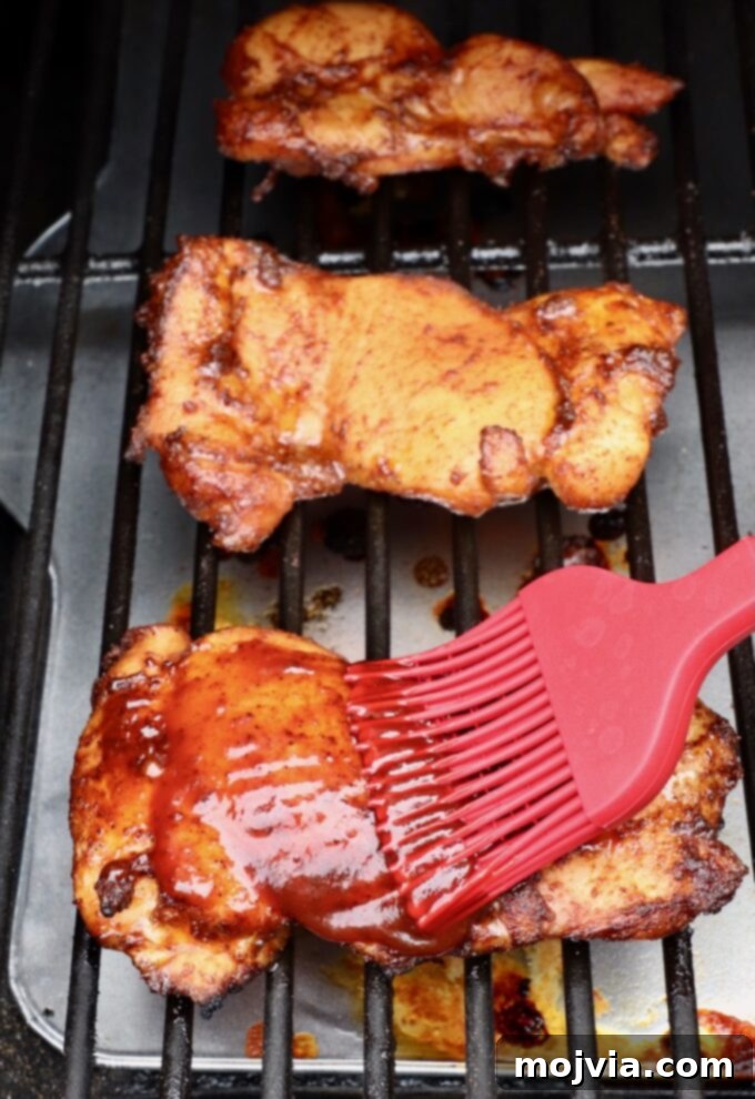 Perfectly Smoked Chicken Thighs 6 chicken thighs brushed with bbq sauce with a red brush on a smoker