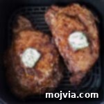 Air Fryer Steakhouse Steak 10 cooked ribeye steaks in an air fryer basket topped with herb compound butter