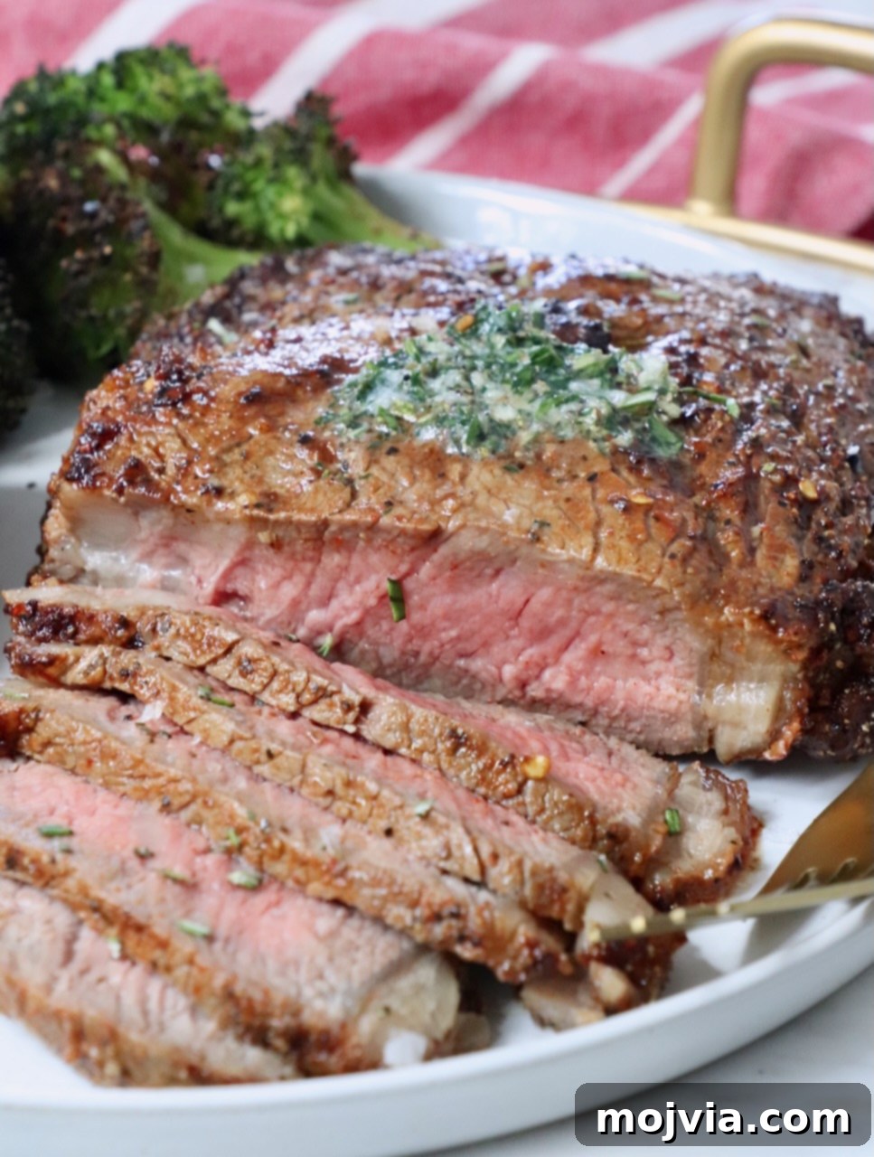 Air Fryer Steakhouse Steak 9 sliced ribeye steak on a plate with herb butter on top of the steak and roasted broccoli in the background on the plate