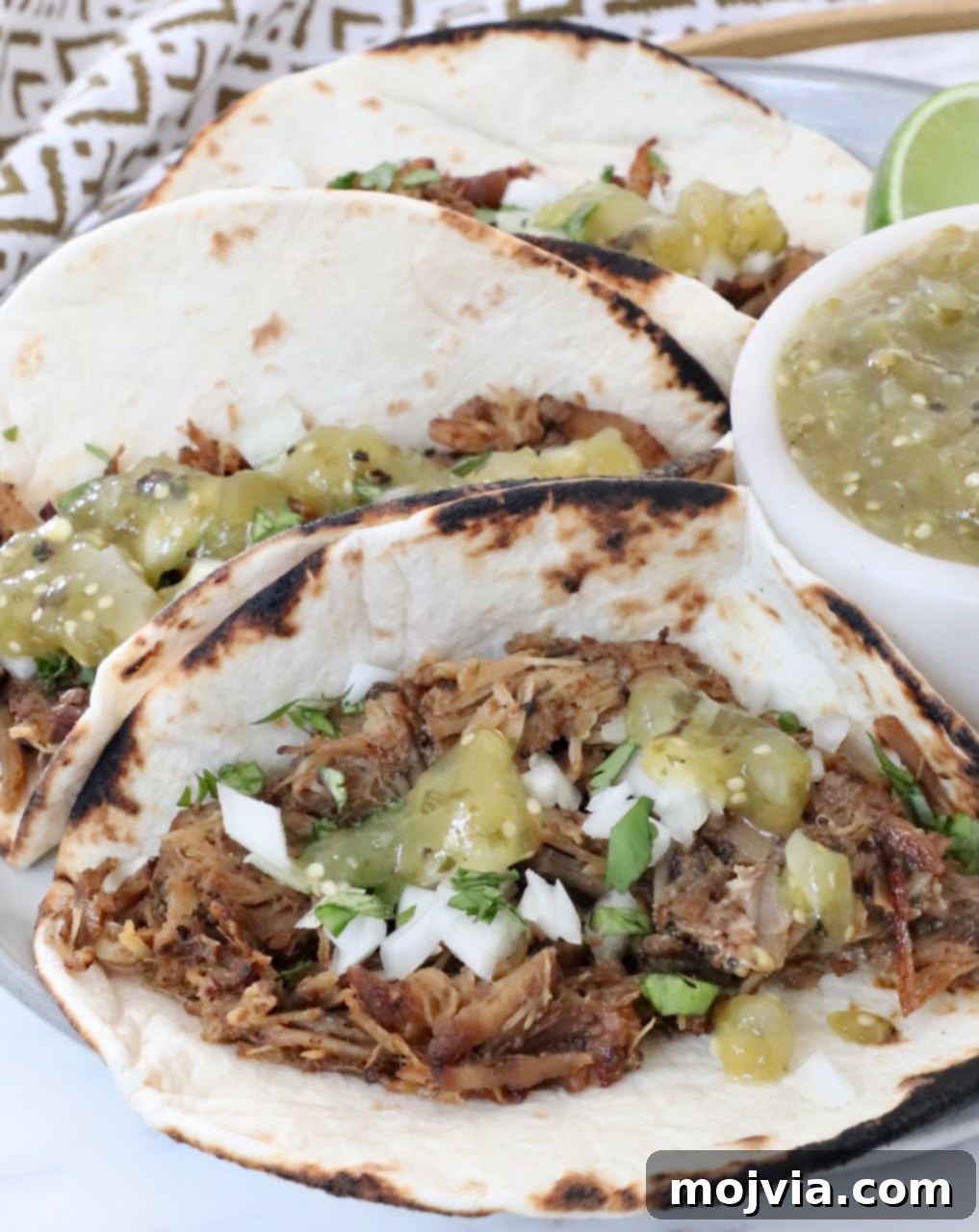 Pork Carnitas 10 carnitas tacos on a plate with tomatillo salsa on the tacos and in a bowl on the side