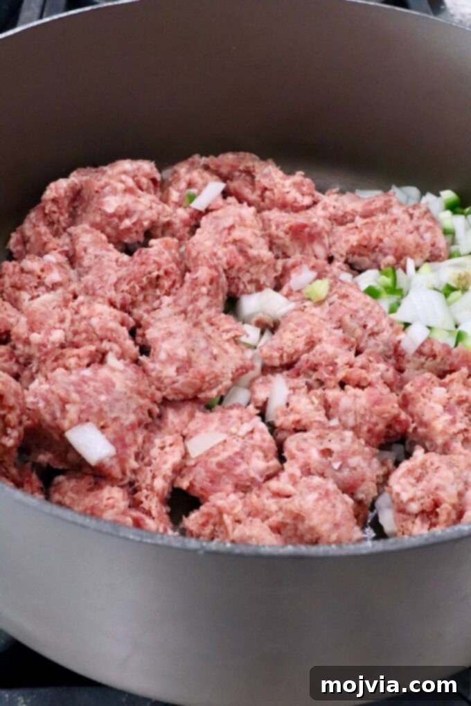 Creamy Smoked Queso 4 uncooked sausage in a large pot with diced onions and jalapenos