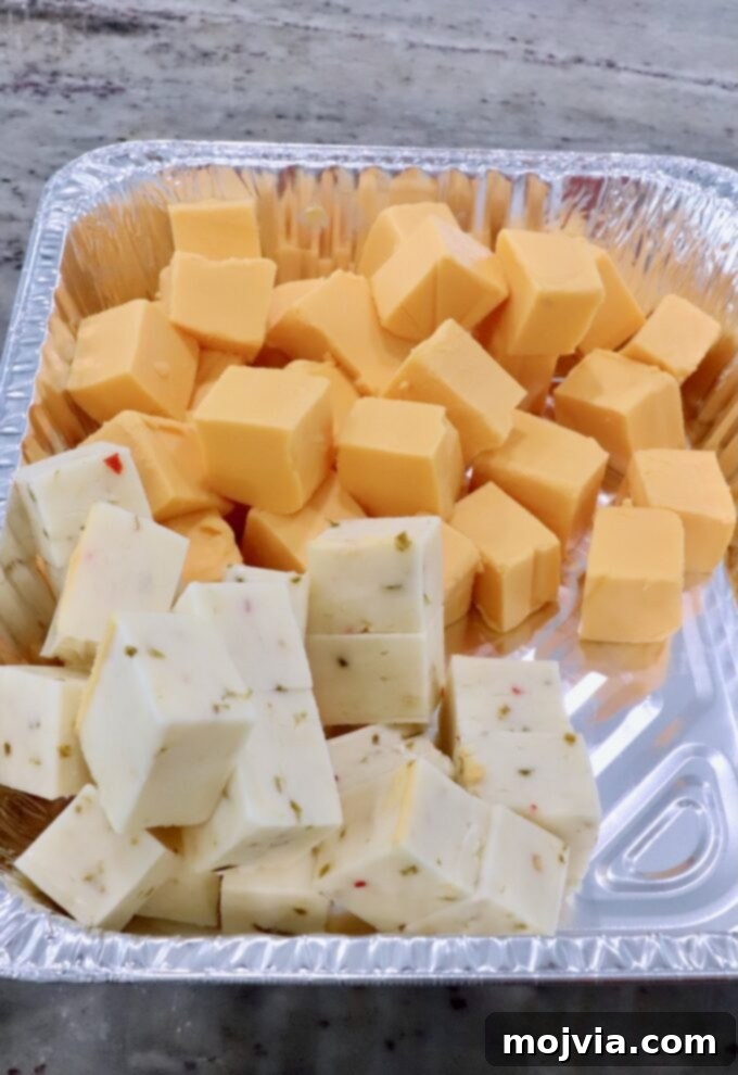 Creamy Smoked Queso 6 cubes of Velveeta cheese and pepper jack cheese in an aluminum foil pan