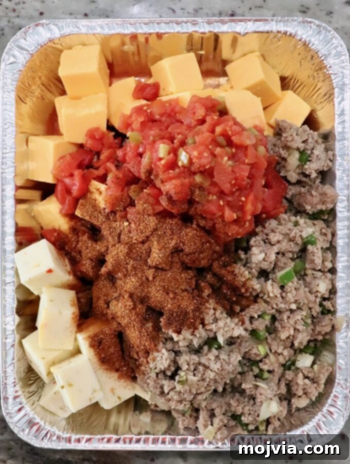 Creamy Smoked Queso 7 cubes of cheese, cooked, crumbled sausage, diced tomatoes and chili seasoning in an aluminum pan