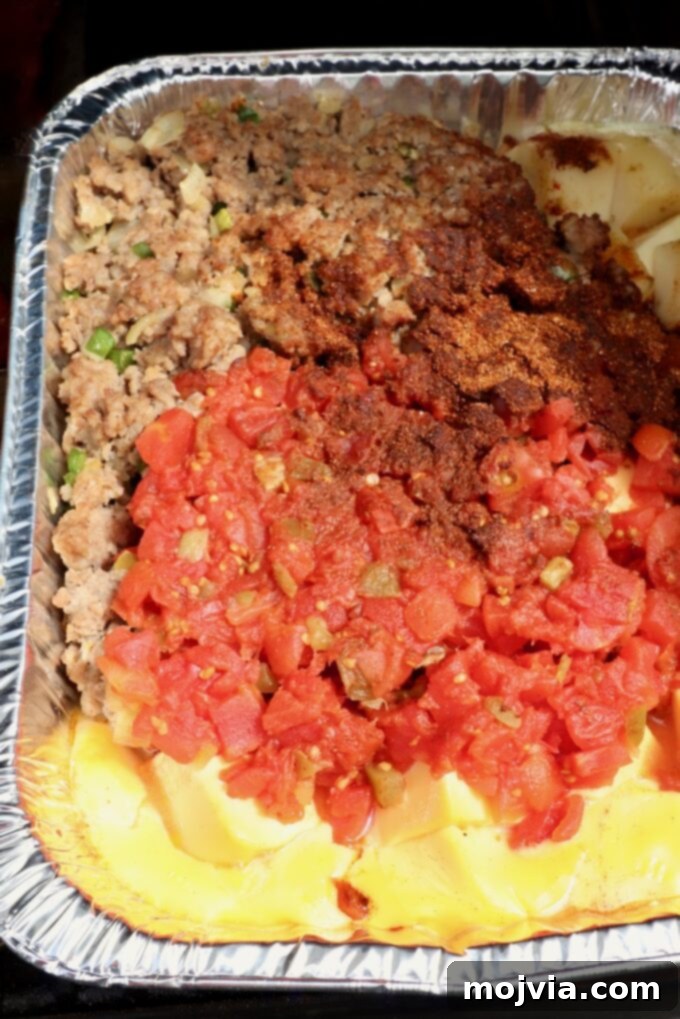 Creamy Smoked Queso 8 melted cheese, cooked, crumbled sausage, diced tomatoes and chili seasoning in an aluminum pan on a smoker