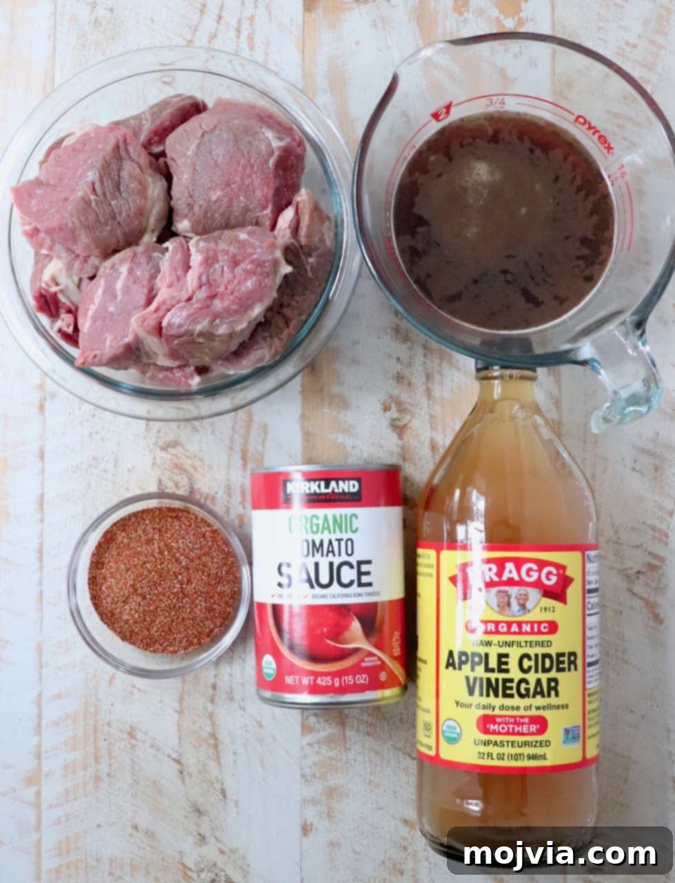 Mouthwatering Instant Pot Birria 3 Ingredients for Instant Pot beef birria laid out on a table, including beef, seasoning, broth, vinegar, and tomato sauce.
