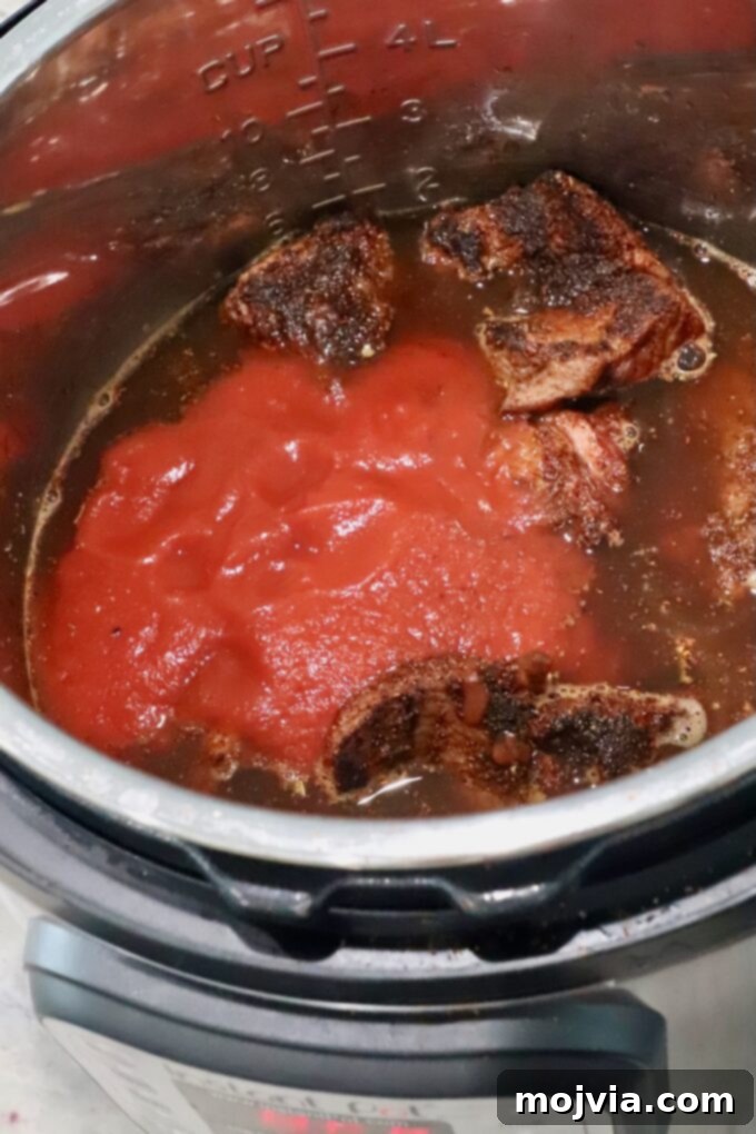 Mouthwatering Instant Pot Birria 6 Seared beef in an Instant Pot, with beef broth and tomato sauce being poured over it, ready for pressure cooking.