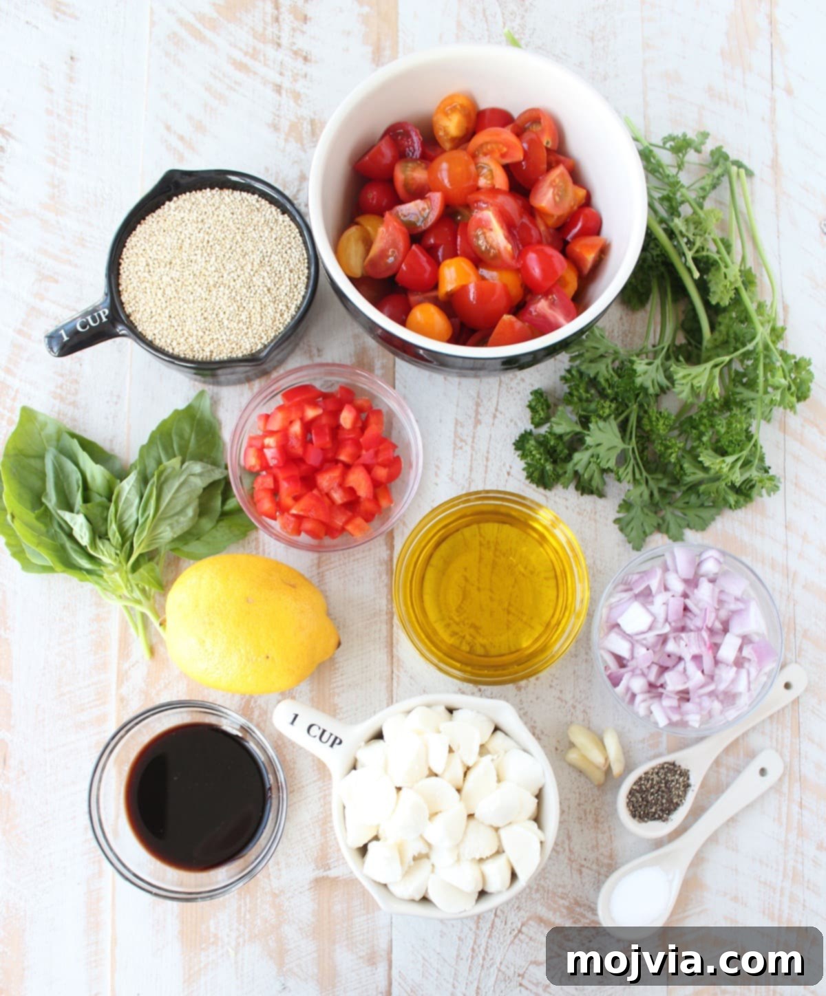 All the fresh ingredients for Quinoa Caprese Salad laid out in separate bowls on a rustic wooden surface.