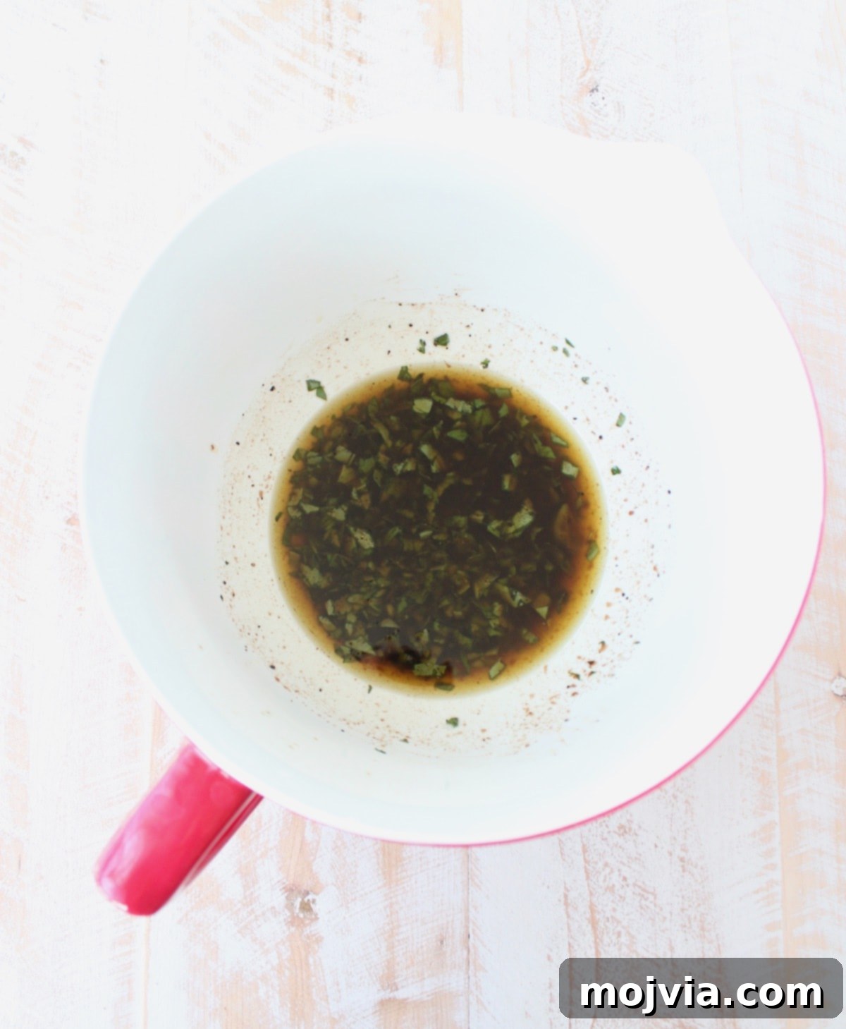 A vibrant bowl containing olive oil, fresh basil, parsley, balsamic vinegar, lemon juice, salt, and pepper, ready to be whisked into a dressing.