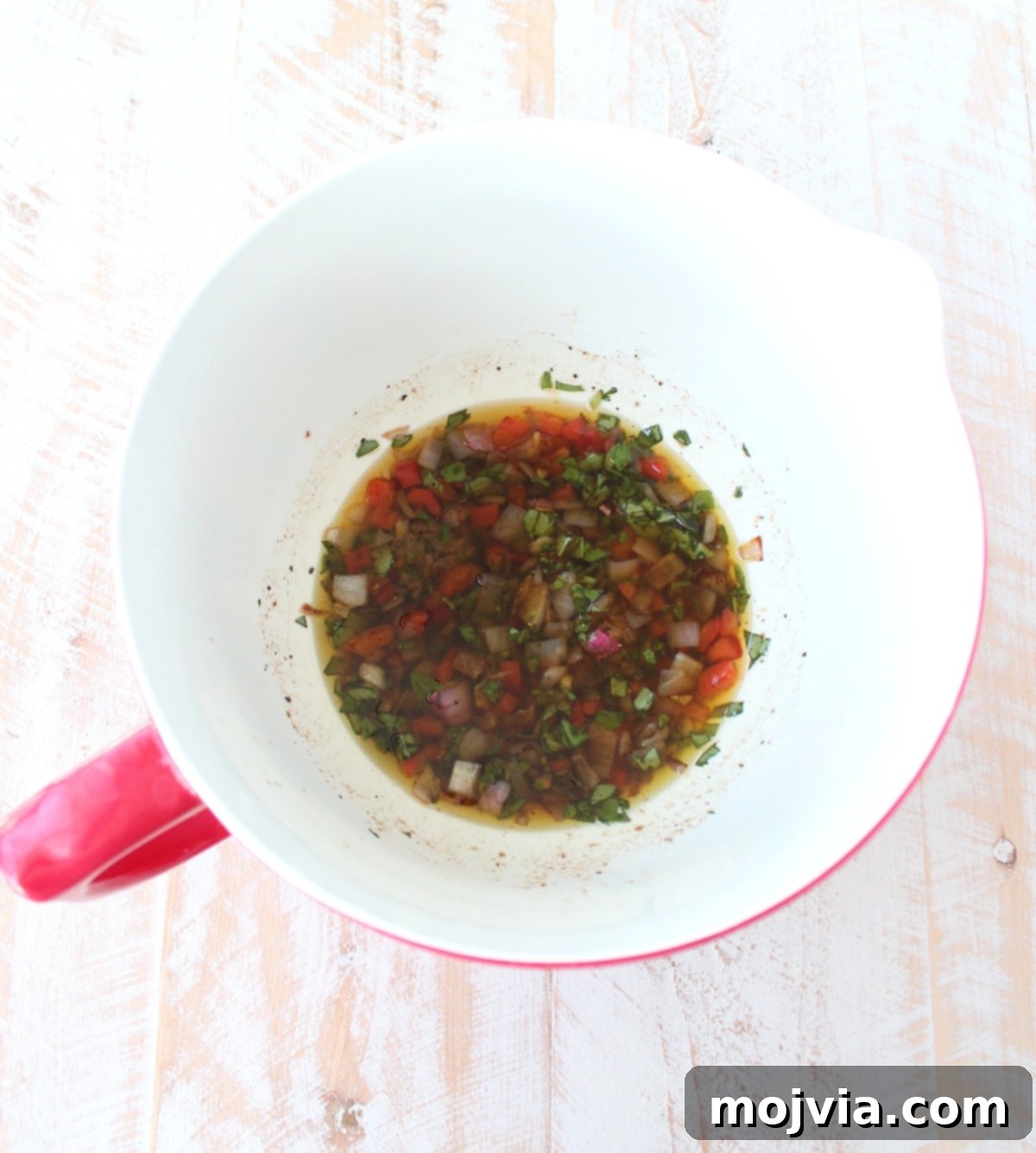 Sautéed onions, peppers, and garlic mixed with the lemon balsamic herb dressing in a white and red bowl.