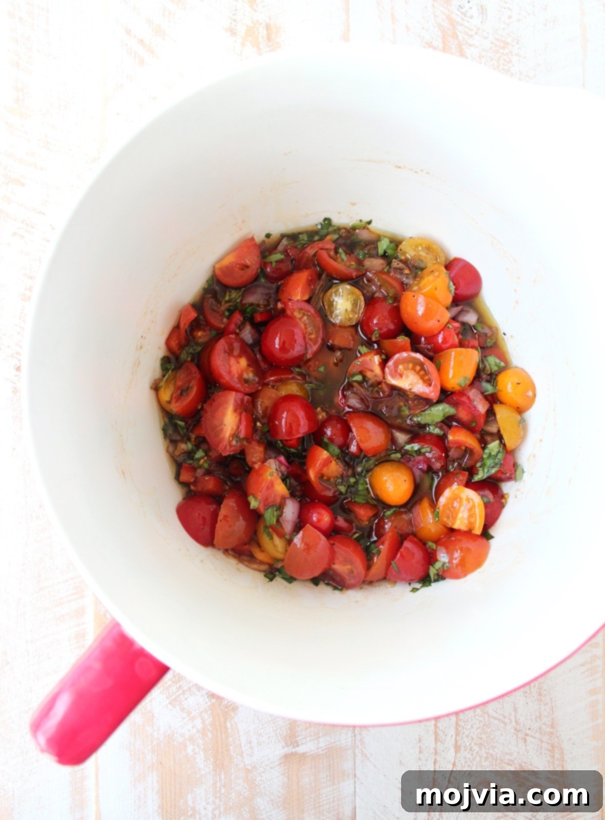Halved cherry tomatoes added to the mixture of onions, peppers, and dressing in a white and red bowl.