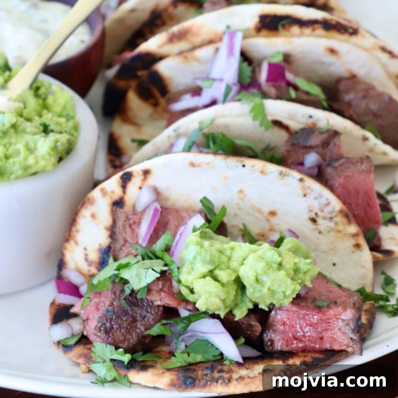 Delicious steak tacos generously topped with creamy guacamole, presented neatly on a plate for a flavorful meal.