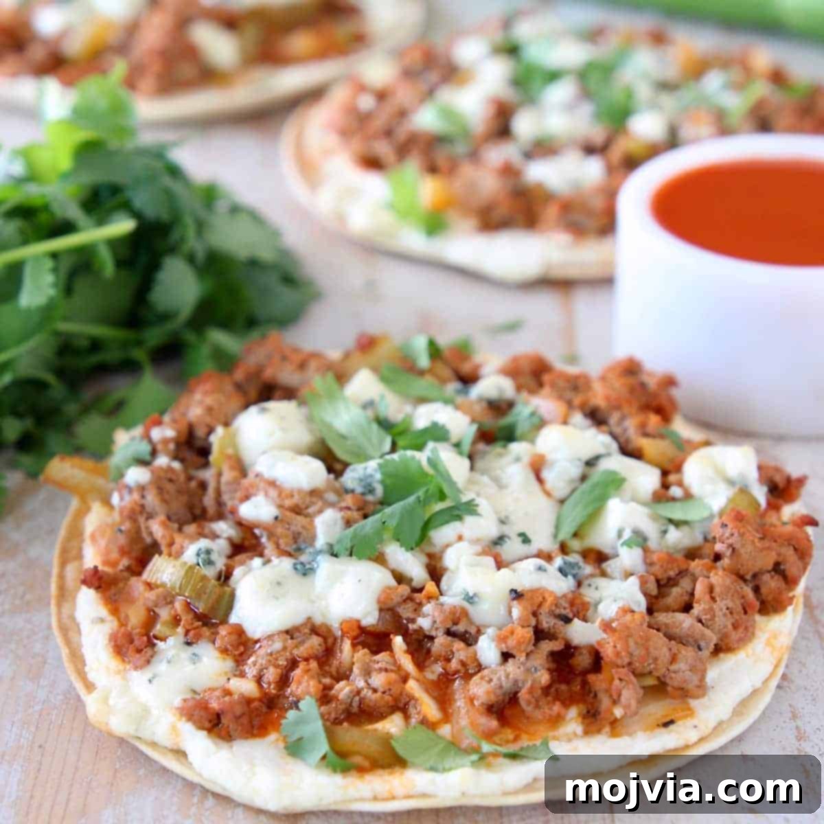 A savory grilled tortilla generously topped with spicy buffalo sauce, seasoned ground turkey, and crumbled blue cheese, showcasing a unique flatbread pizza.