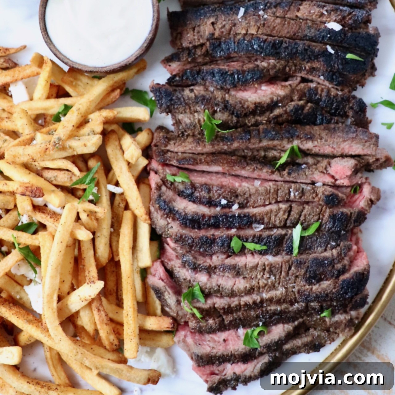 A platter featuring tender, thinly sliced beef shawarma, accompanied by a side of crispy french fries and a small bowl of creamy dipping sauce.