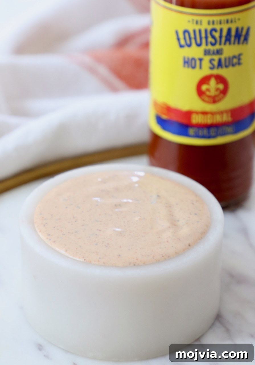 Bold Louisiana Cajun Sauce 2 creamy cajun sauce in a small white bowl with a bottle of hot sauce behind it