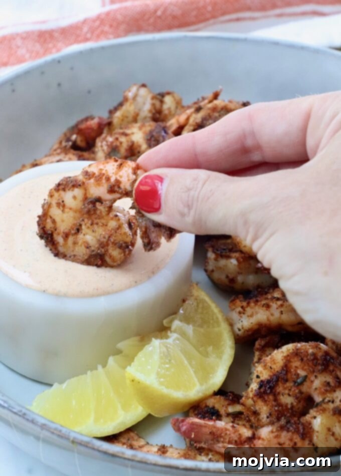 Bold Louisiana Cajun Sauce 5 hand dipping a cooked shrimp into a bowl of creamy sauce